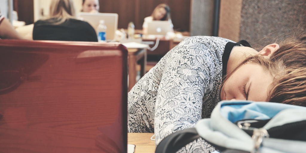 Une jeune femme pose sa tête sur son sac à dos dans une bibliothèque.